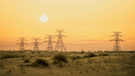 Tralicci elettrici e linee di alta tensione in controluce contro un cielo dorato al tramonto
