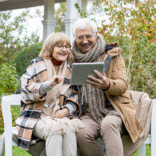 Two people sitting on a bench outdoors sharing a tablet device.