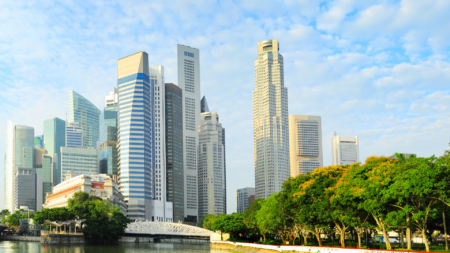 Panorama urbano di Singapore con moderni grattacieli e un'area verde lungo il fiume, sotto un cielo parzialmente nuvoloso