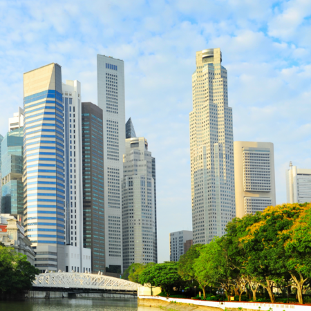 Panorama urbano di Singapore con moderni grattacieli e un'area verde lungo il fiume, sotto un cielo parzialmente nuvoloso
